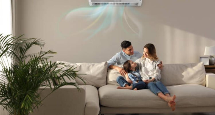 Happy family resting under air conditioner on beige wall at home